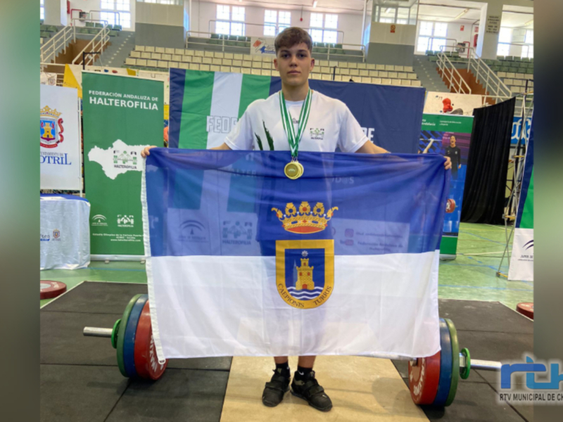 Un atleta levanta una bandera con el escudo de Chipiona, posando orgulloso en un gimnasio deportivo.