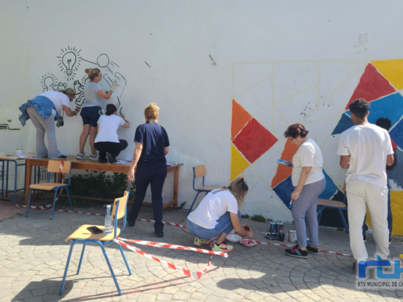 Grupos de personas trabajando juntos en un mural colaborativo en una pared exterior.