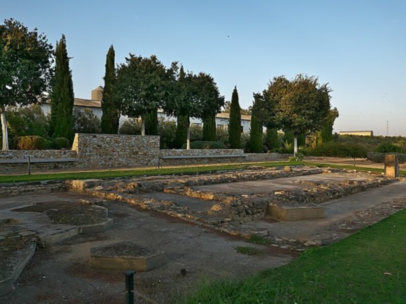 Ruinas históricas con jardín y edificio en el fondo al atardecer.