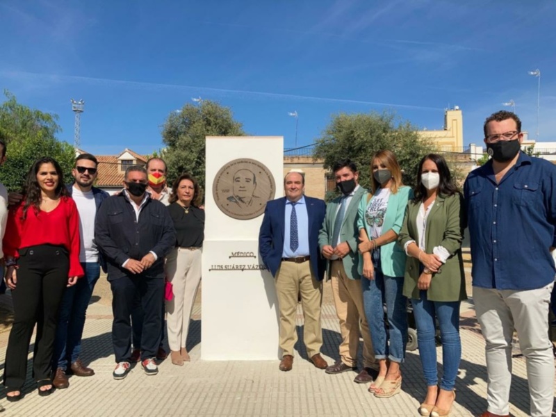 Gente posando junto a una placa con texto en español, posiblemente en un evento o celebración oficial. Todos están vestidos formalmente y algunos llevan mascarillas. El contexto sugiere una ceremonia o reconocimiento público.
