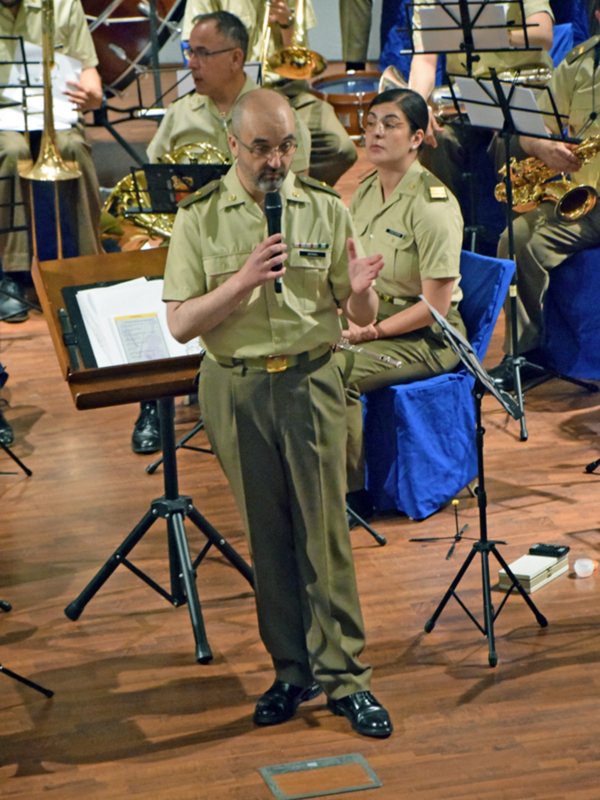 Un hombre en uniforme militar está hablando en un micrófono mientras una mujer en uniforme militar mira hacia él.