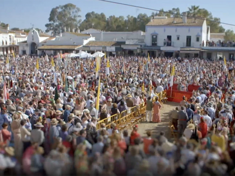 Una multitud de personas reunidas en una plaza pública, con banderas y trajes tradicionales, en un evento festivo o ceremonial.
