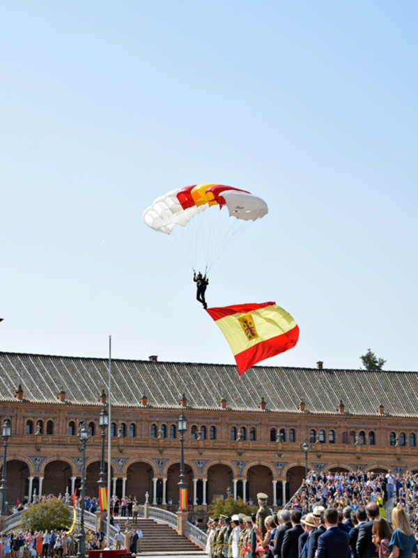 Paracaidistas militares desciendo con una bandera española en un desfile militar en España.