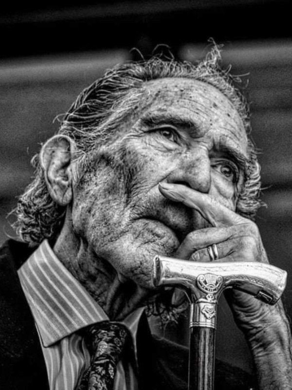 Retrato en blanco y negro de un anciano pensativo sosteniendo un bastón.
