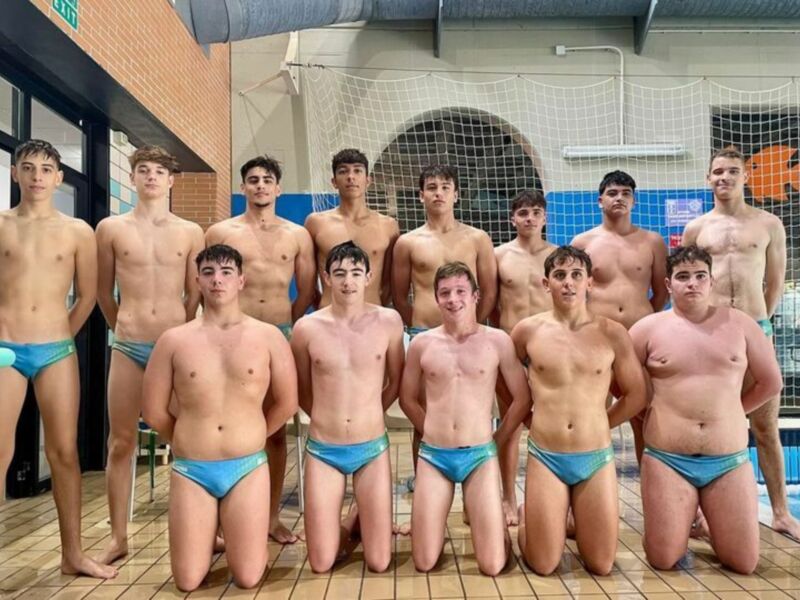 Equipo de natación masculino posando en una piscina cubierta.