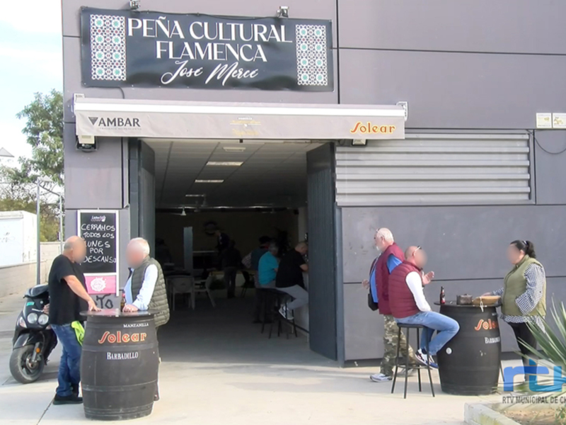 Entrada a la Peña Cultural Flamenca José Merce, donde personas disfrutan de la música y la cultura flamenca al aire libre.