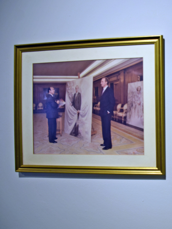 Dos hombres en trajes de negocios despliegan un lienzo en un salón clásico con decoración elegante.
