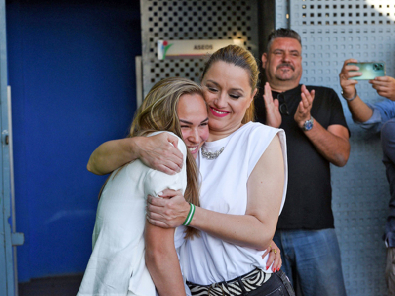 Festejo entre dos mujeres abrazándose, rodeadas por un grupo de personas que aplauden.