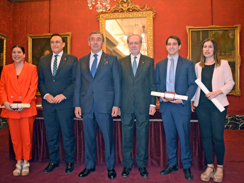 Una celebración formal en un entorno elegante, con personas vestidas con trajes y una mujer con un vestido naranja, posando para la foto.