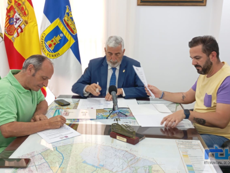 Una reunión formal donde tres personas están sentadas alrededor de una mesa, con documentos y una bandera en el fondo. La escena sugiere una reunión de negociación o firma de un acuerdo.