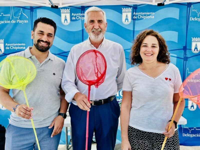 Tres personas sonrientes con redes de pesca, en un evento de la Delegación de Playas del Ayuntamiento de Chipiona.