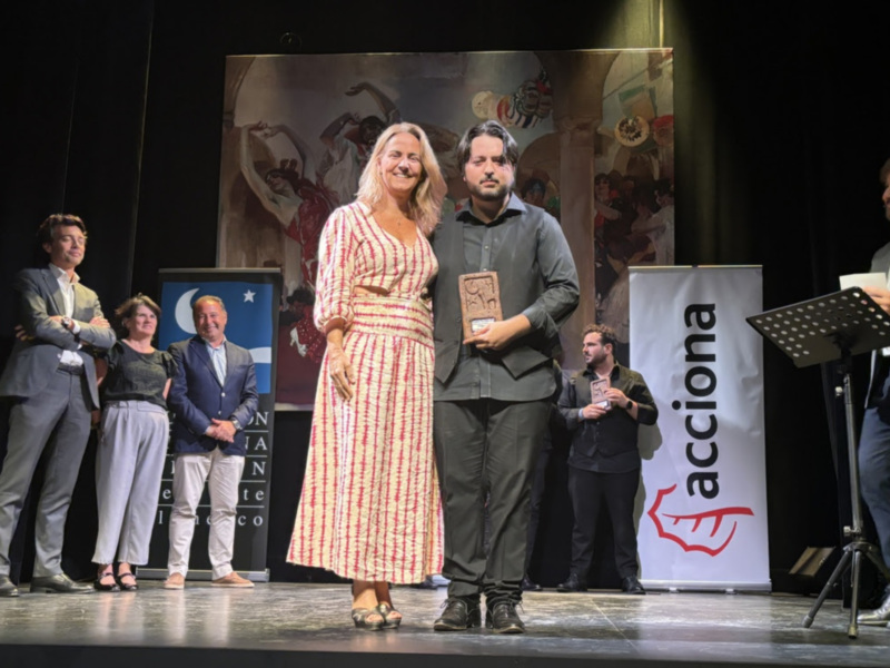 Premio en una ceremonia de entrega de galardones en un escenario con un fondo artístico y el logo de Acciona en el fondo.
