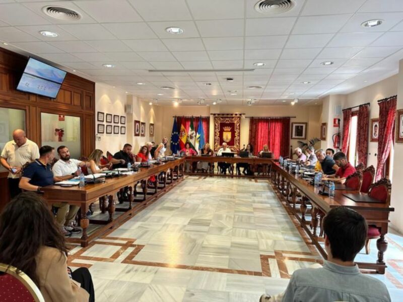 Sala de reuniones con mesas largas, personas sentadas, banderas y decoración oficial.