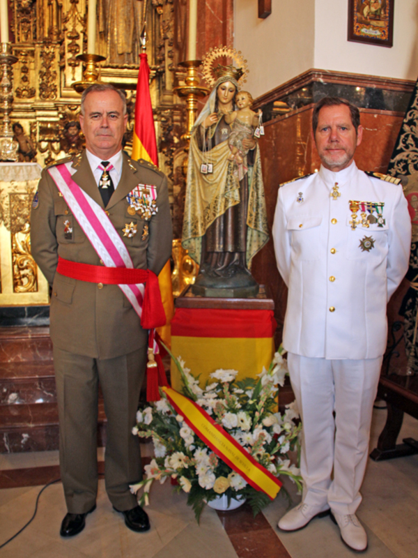Oficiales militares en uniforme ceremonial posando frente a una estatua de la Virgen del Carmen en una iglesia.
