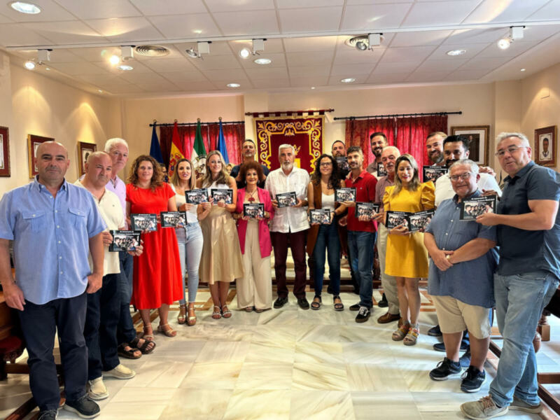 Grupo de personas posando con libros en una sala decorada con banderas y tapices.