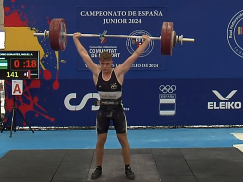Atleta levantando pesas en el Campeonato de España Junior 2024, con marcador de tiempo y listado de atletas en el panel izquierdo.