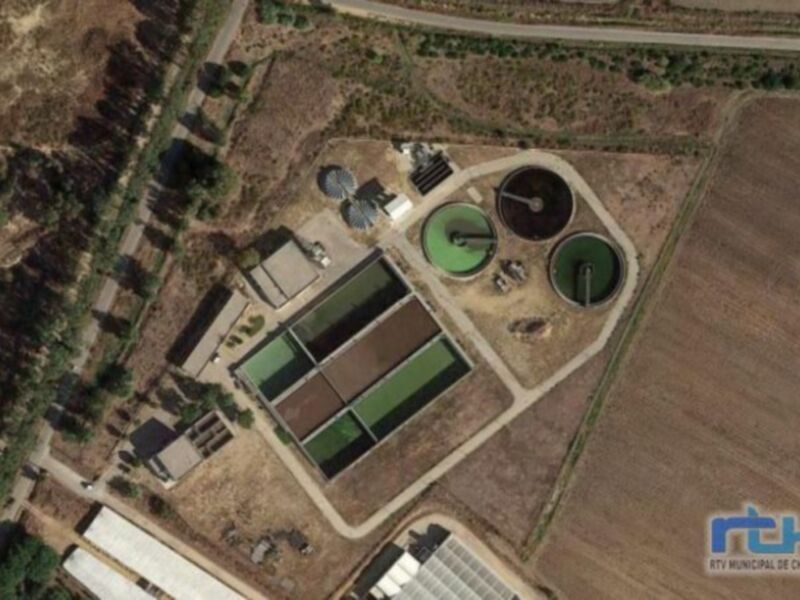 Planta de tratamiento de aguas residuales vista desde arriba, rodeada de campos y árboles.