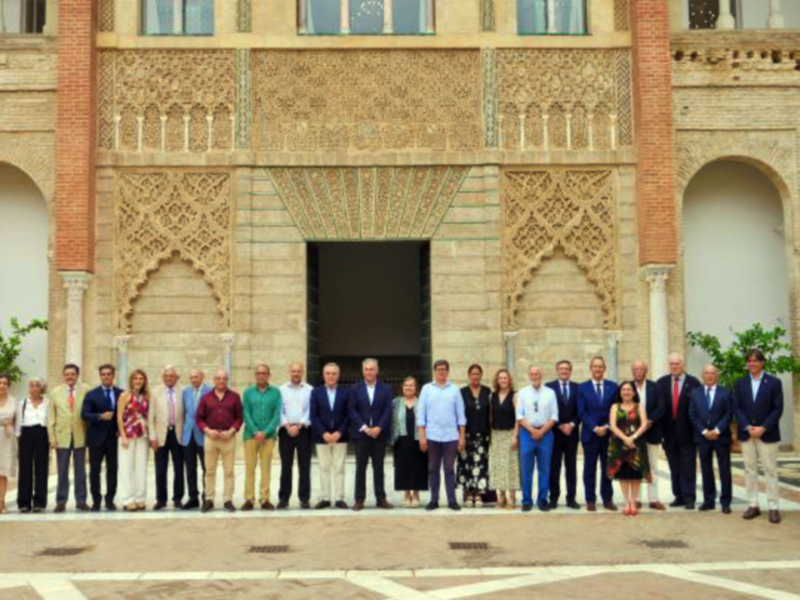 Gruppo di persone in abiti formali posano per un'immagine di gruppo davanti a un palazzo storico con archi e decorazioni.