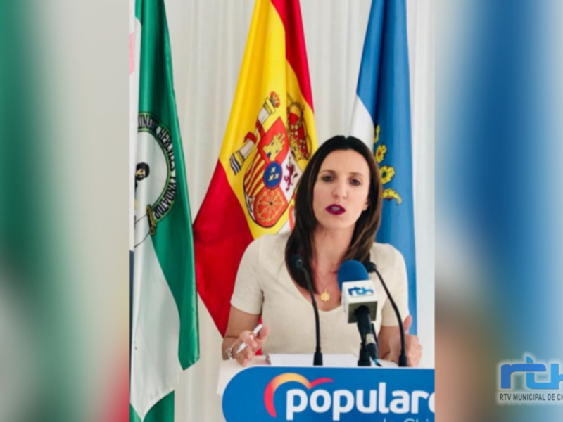 Mujer hablando en rueda de prensa con banderas de España y Andalucía en el fondo.