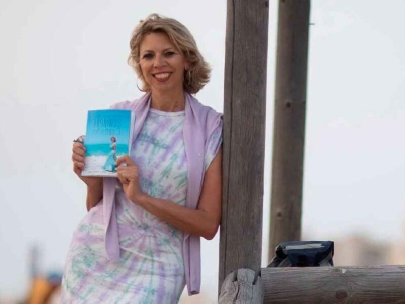 Autora con libro en la playa, ambiente relajado.