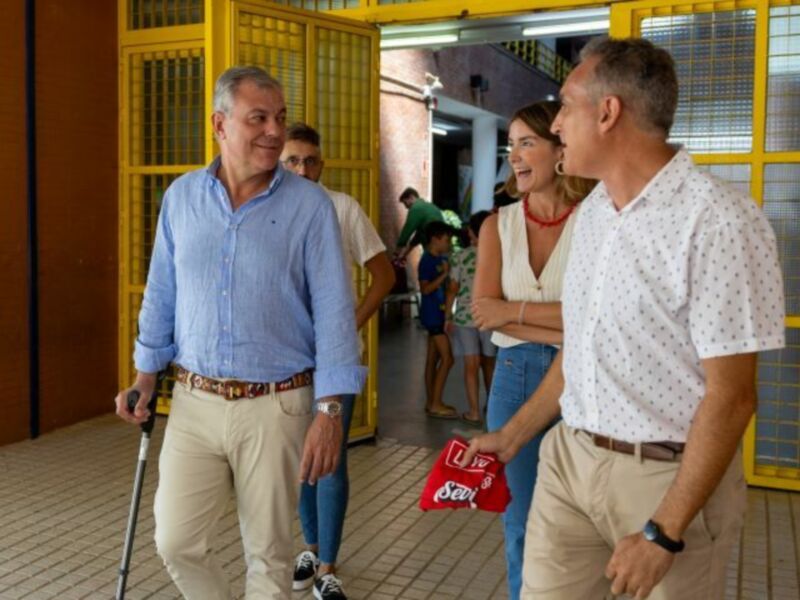 Personas intercambiando saludos en un corredor con puertas amarillas y muros de ladrillo.