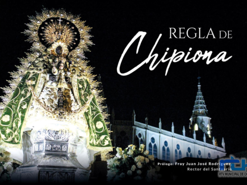 Virgen de Chipiona en procesión nocturna, adornada con elegantes vestimentas y guirnaldas de flores, frente a la catedral iluminada.