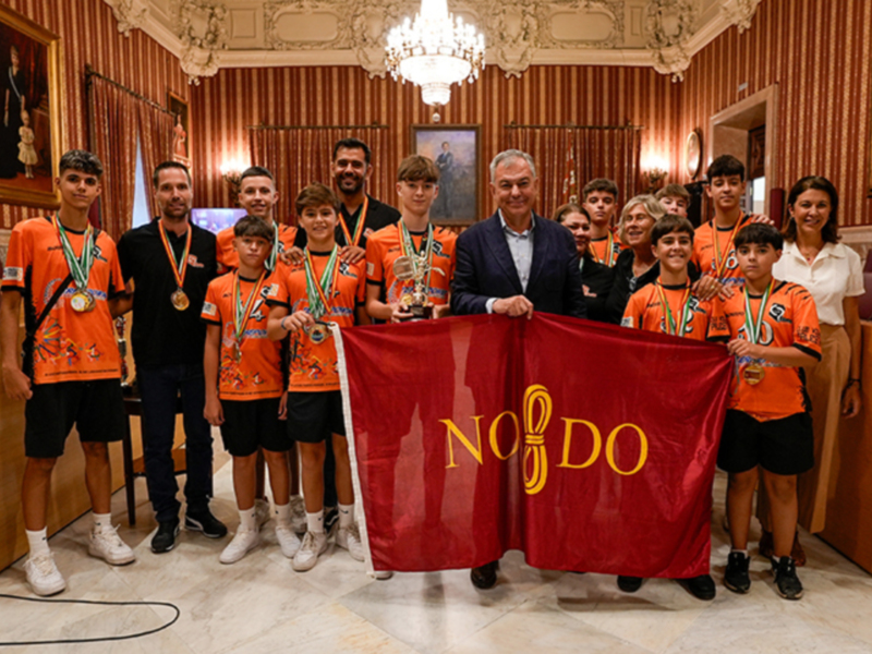 Equipo deportivo con medallas y bandera de NO DO celebrando en un salón con decoración clásica.