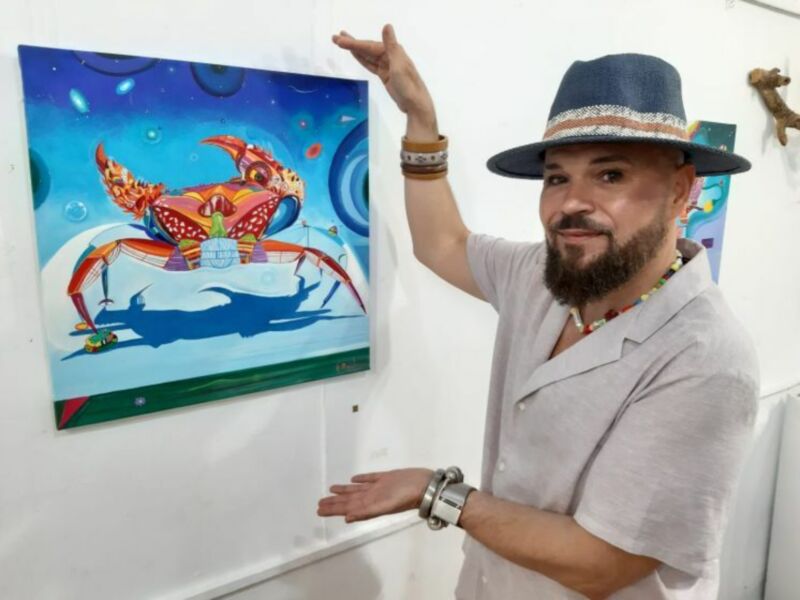 Artista presentando su obra abstracta con un cangrejo en un mar de colores vibrantes.