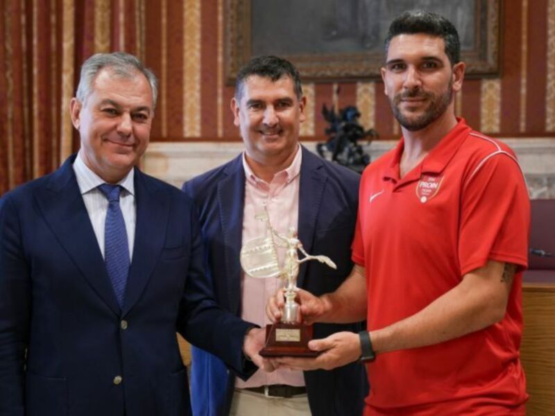 Premio recibido por un atleta en un evento deportivo, junto a dos personas importantes en la ceremonia.