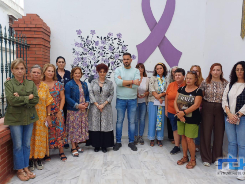 Gruppo di persone in posa davanti a un murale con nastro viola e fiori viola, simbolo di consapevolezza sul cancro al seno.