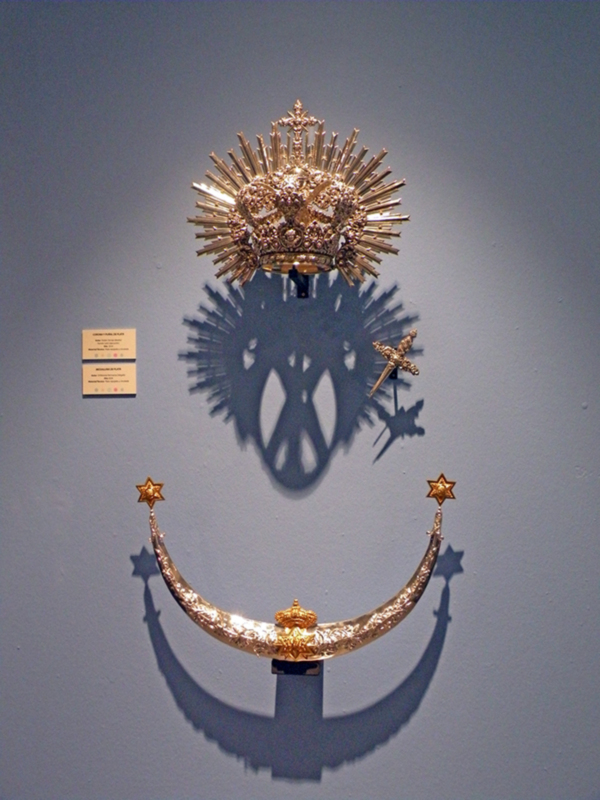 Reproducción de la Corona de la Reina de la Plata, expuesta en un museo con su sombra proyectada en la pared.