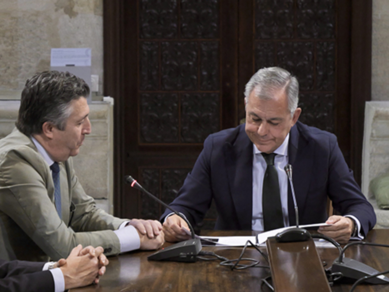 Reunión de negocios en un entorno formal con tres hombres en trajes discutiendo en una mesa de conferencias.
