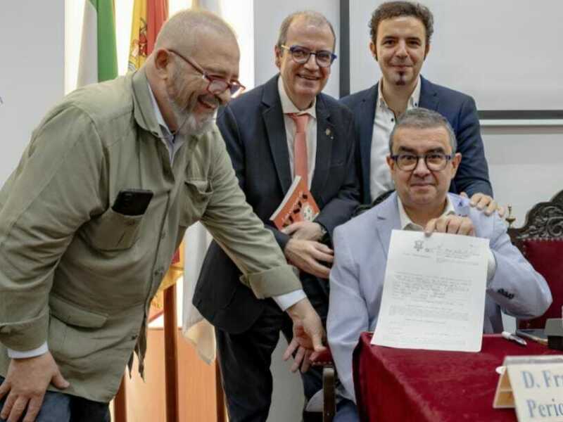 Un grupo de personas en una reunión formal, con uno de ellos sosteniendo un documento y sonriendo. En el fondo, se pueden ver banderas y una silla de oficina.