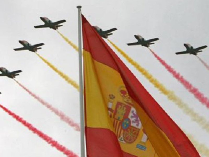 Aviones militares en formación con banderas españolas y colas de humo en el cielo.