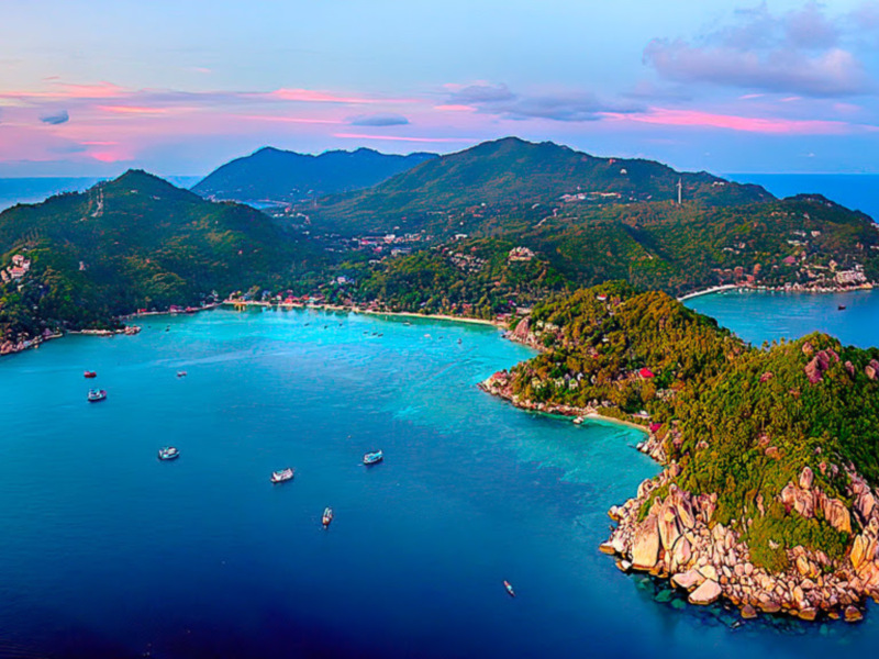 Isla tropical con montañas verdes y agua turquesa al atardecer.