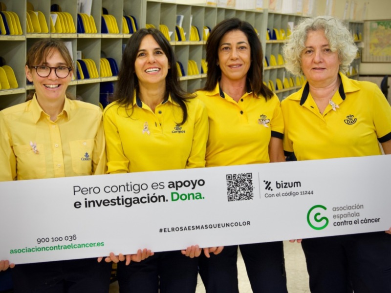 Cuatro mujeres sonríen mientras sostienen un letrero promoviendo donaciones para la investigación del cáncer.