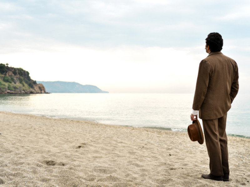 Persona en traje de negocios observando el horizonte del mar en una playa desierta.