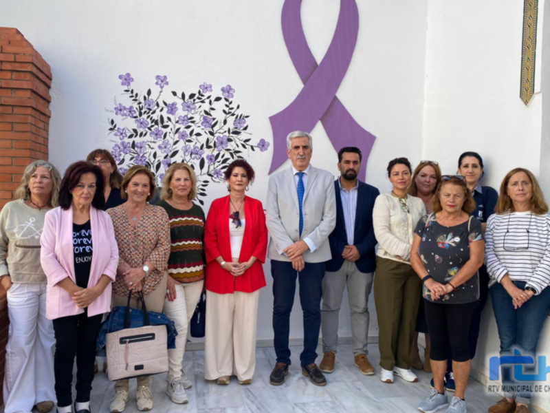Grupal de personas frente a un mural con un lazo violeta y flores, probablemente en un evento de concienciación sobre la violencia de género.