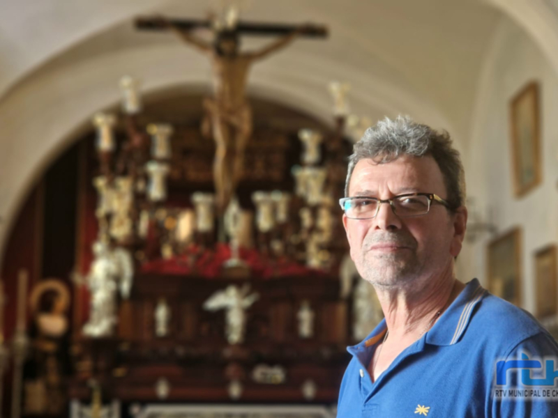 Hombre en una iglesia, detrás de un altar con estatuas y una figura del Cristo crucificado.