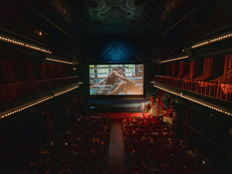 Interior de un cine con proyección en pantalla y público en la sala.