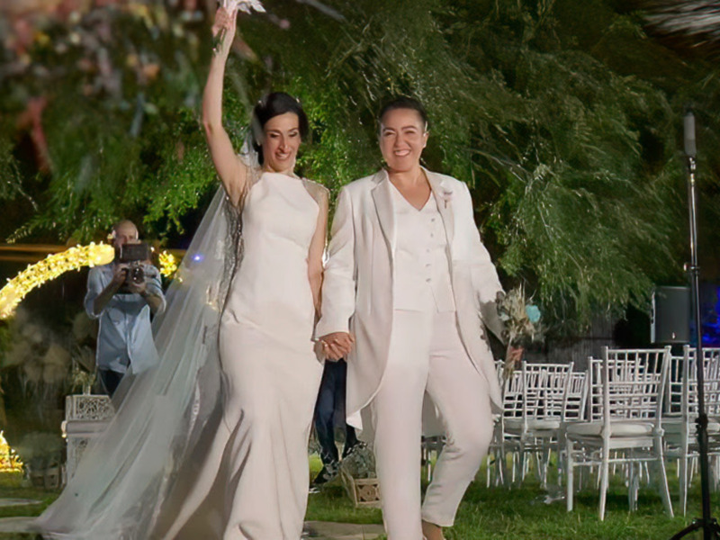 Novias celebrando su boda al aire libre bajo una arco floral iluminado.