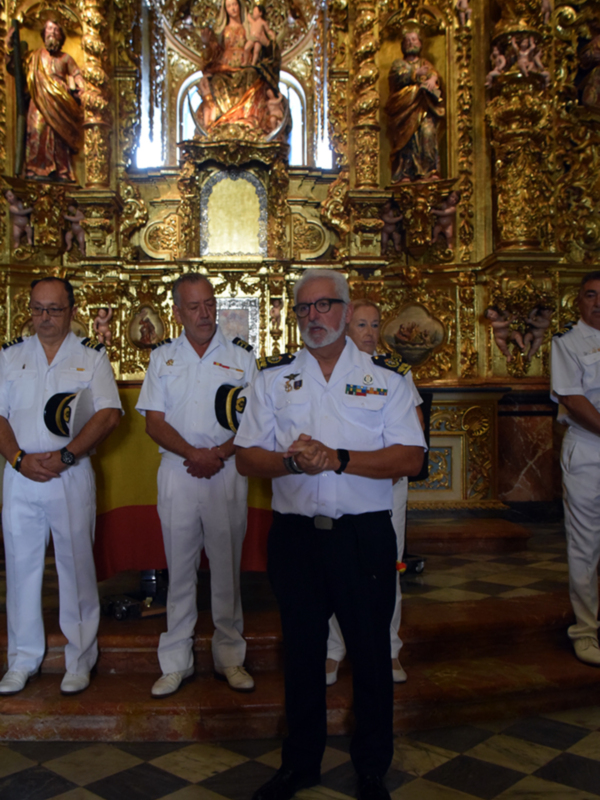 Oficiales en uniforme blanco frente a un retablo dorado en una iglesia.
