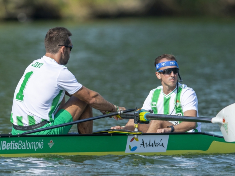 Atletas en barco de remo del Real Betis Balompié compitiendo en un evento acuático.