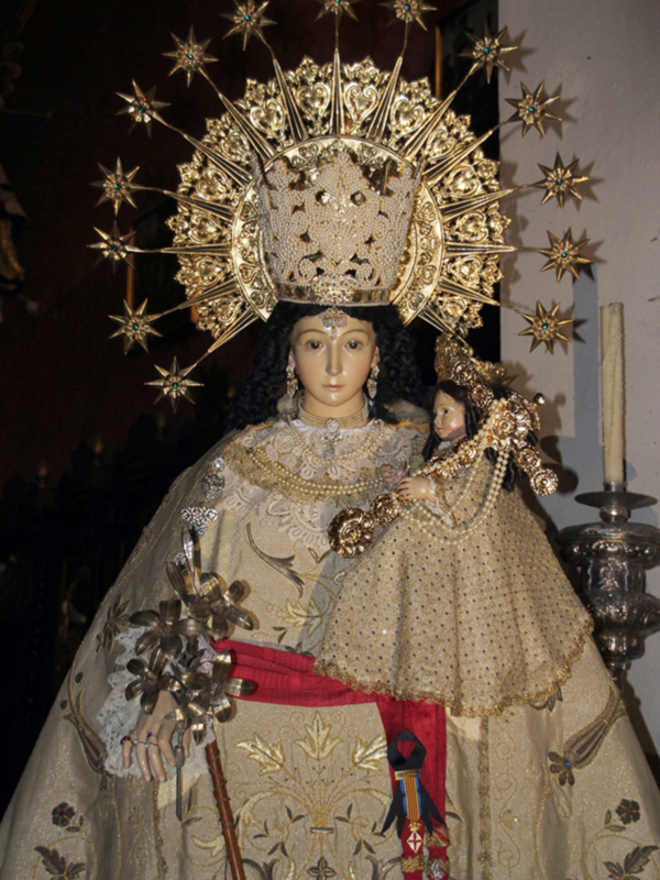 Imagen de una estatua de la Virgen María con una corona de estrellas doradas y una vestimenta ornada con detalles dorados y perlas.