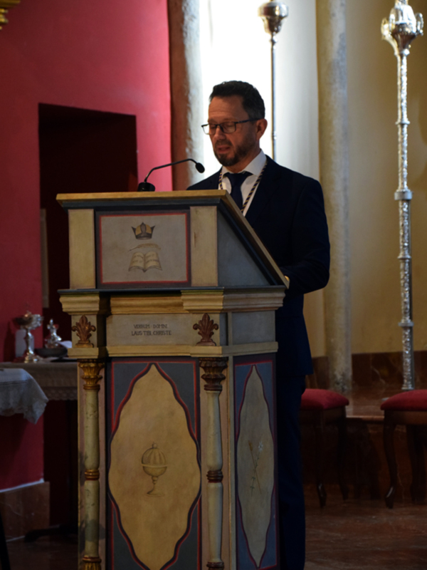 Persona hablando desde un púlpito decorado en un interior religioso.
