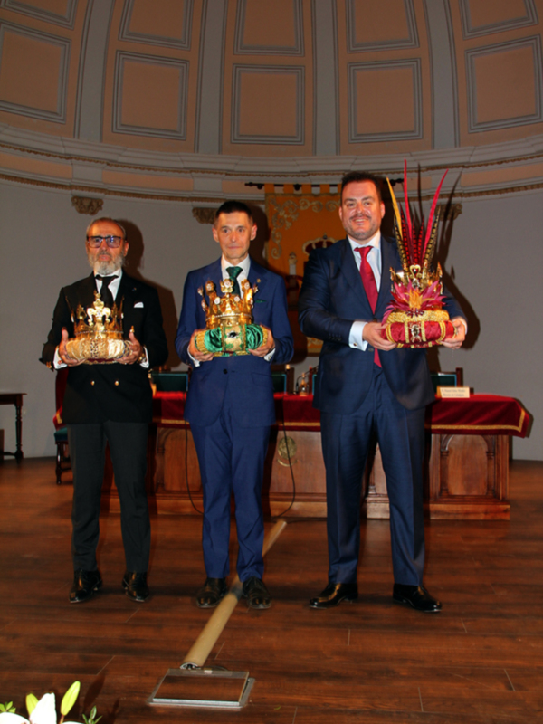 Tres hombres en trajes formales sostienen trofeos decorativos en una ceremonia formal.