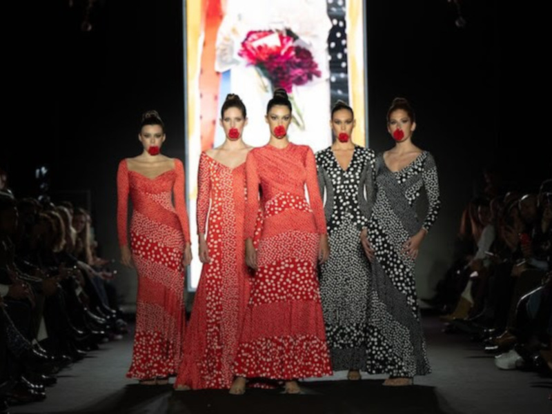 Desfile de moda con modelos en vestidos de lunares y rojos en un pasarela iluminada.