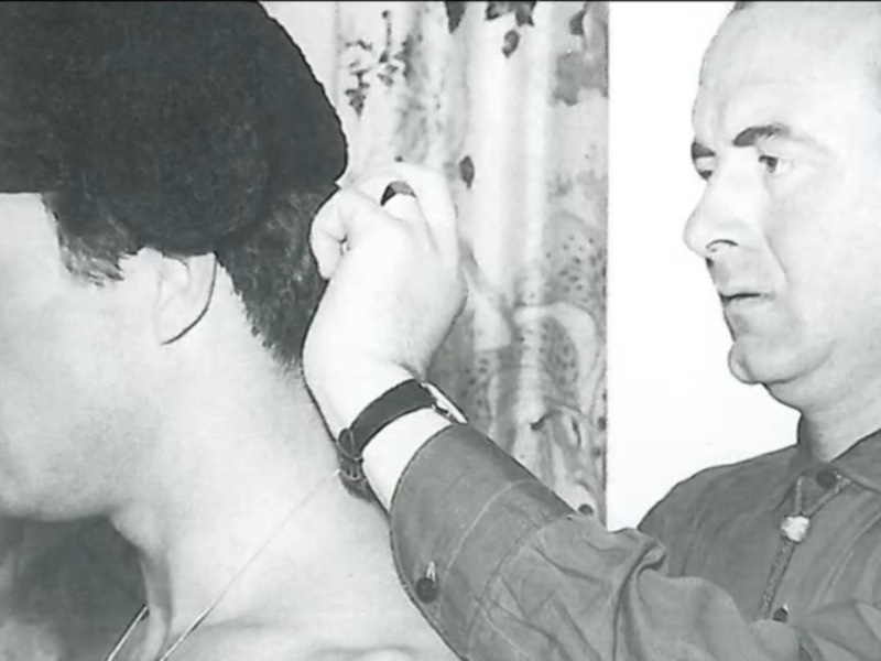 Un hombre está peinando el cabello de otra persona, ambas en blanco y negro.