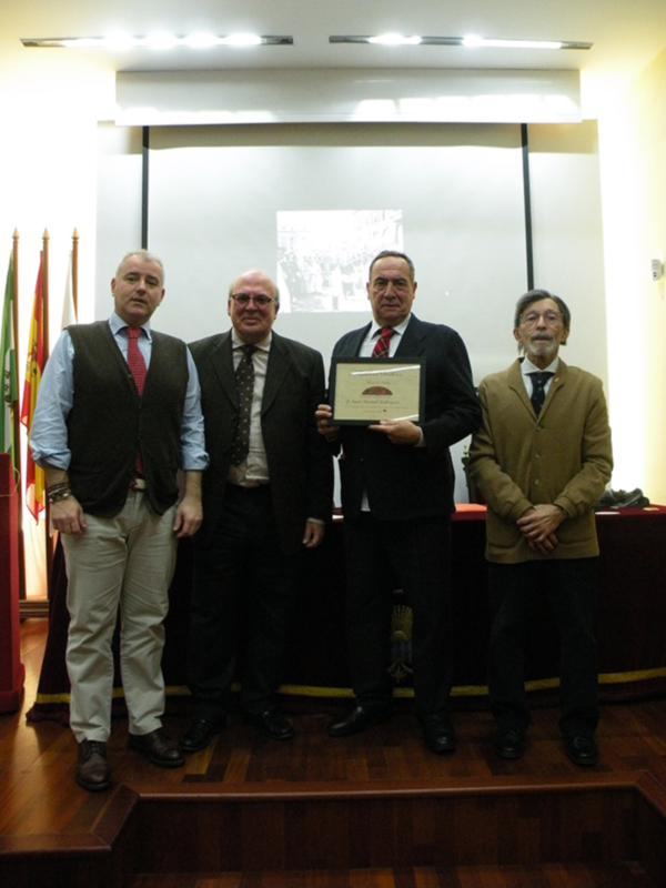 Premio otorgado en ceremonia oficial en un salón con banderas y proyección en fondo.