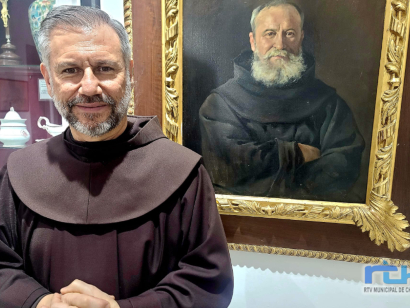 Monje franciscano posa frente a un retrato de un monje franciscano en un museo.
